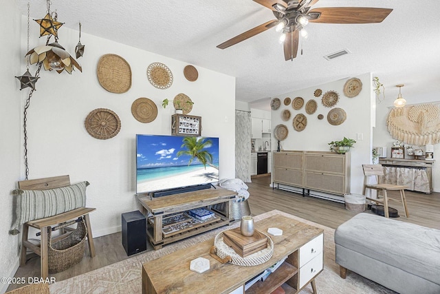 living area with a textured ceiling, wood finished floors, visible vents, baseboards, and a ceiling fan