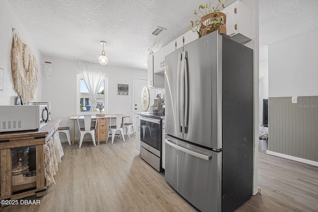 kitchen featuring a textured ceiling, stainless steel appliances, light wood finished floors, and visible vents