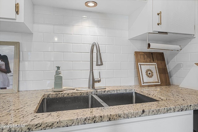 kitchen with white cabinets, light stone counters, decorative backsplash, and a sink