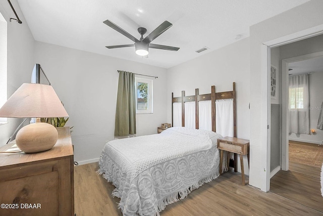 bedroom featuring visible vents, ceiling fan, baseboards, and wood finished floors