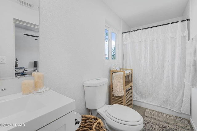 bathroom featuring visible vents, a textured wall, a shower with shower curtain, toilet, and vanity