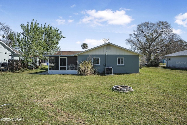 back of property with cooling unit, a sunroom, a lawn, and an outdoor fire pit