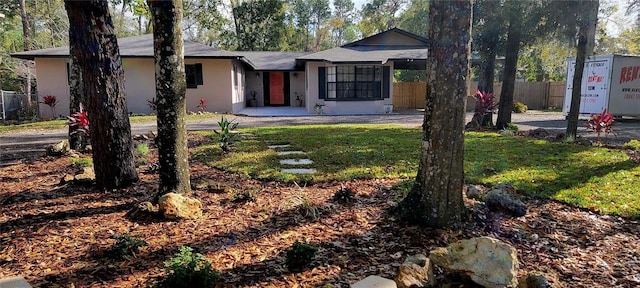 view of front of house with stucco siding, a front lawn, and fence