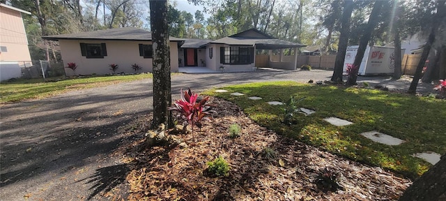 view of front facade featuring stucco siding, driveway, a front lawn, and fence