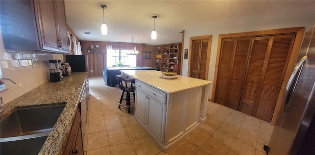 kitchen featuring decorative light fixtures, light tile patterned floors, tasteful backsplash, a sink, and a kitchen island