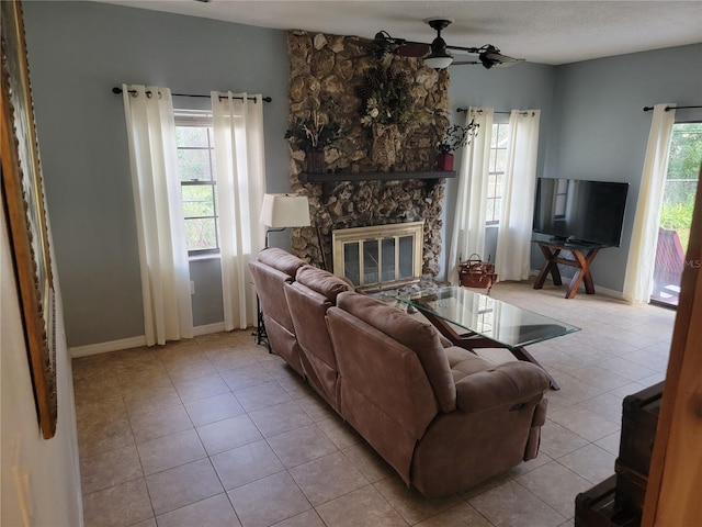 living room featuring plenty of natural light, a ceiling fan, and a stone fireplace