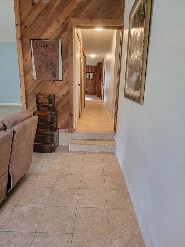 corridor with light tile patterned floors, baseboards, and wooden walls