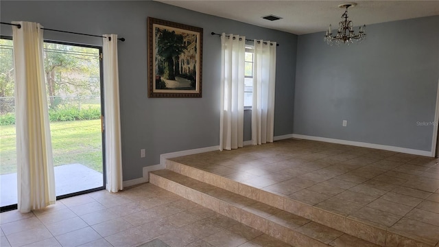 empty room with a chandelier, light tile patterned flooring, visible vents, and baseboards