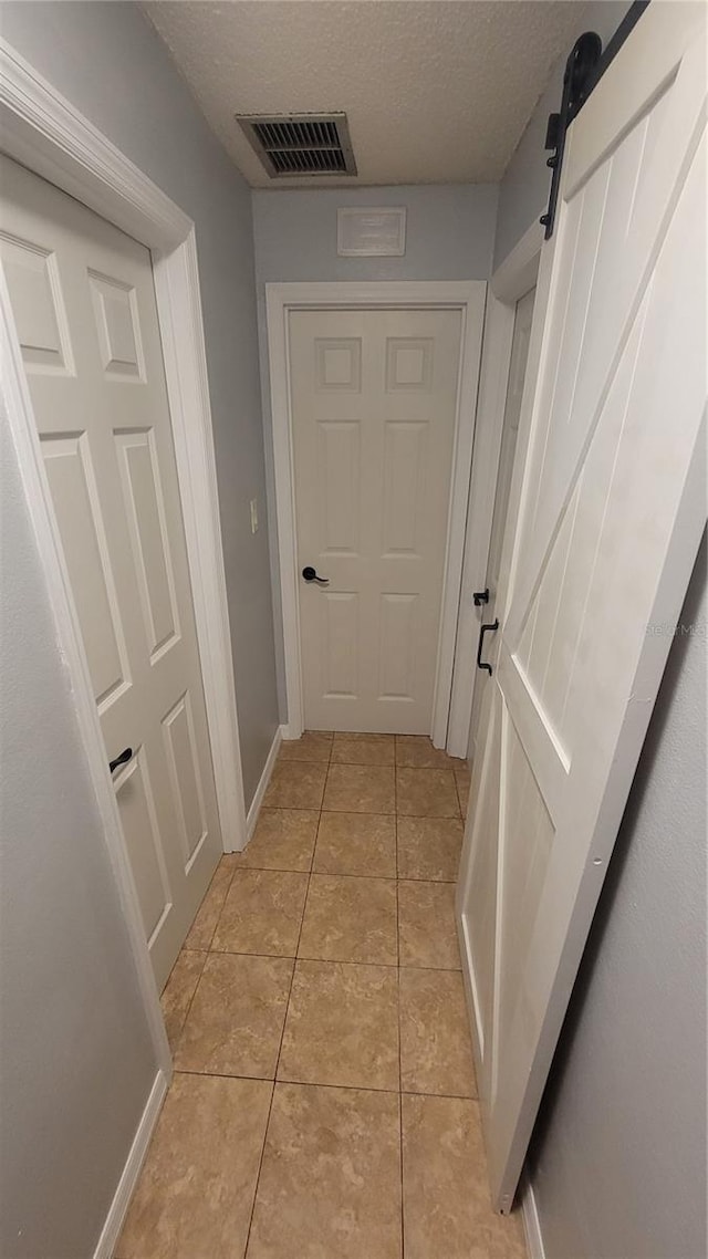 hallway with visible vents, a barn door, light tile patterned flooring, a textured ceiling, and baseboards