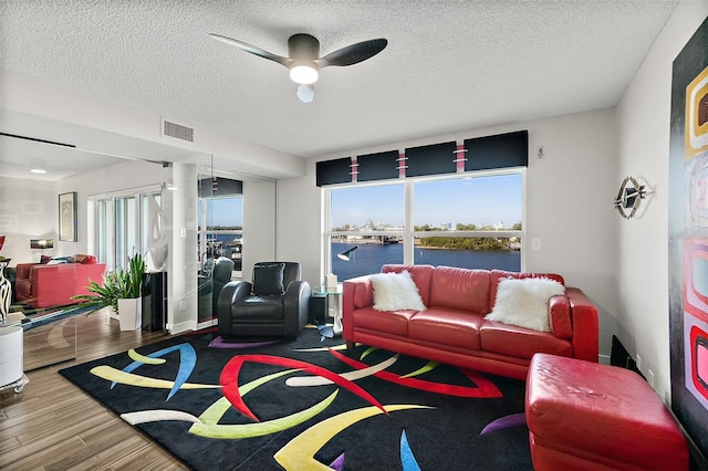 living room featuring a water view, visible vents, ceiling fan, a textured ceiling, and wood finished floors