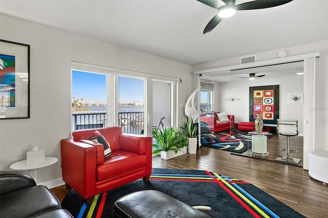 living area with a ceiling fan, wood finished floors, visible vents, and a healthy amount of sunlight