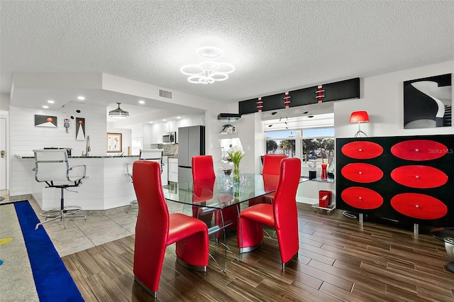 dining area with a textured ceiling, an inviting chandelier, visible vents, and wood tiled floor