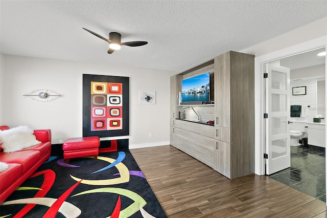 living room featuring dark wood-style floors, ceiling fan, a textured ceiling, and baseboards