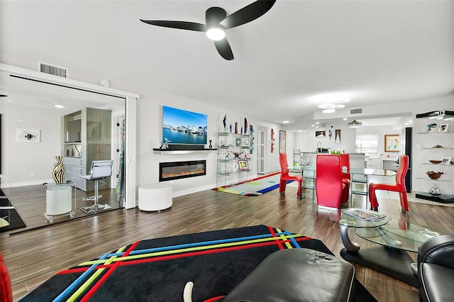 living area with a glass covered fireplace, visible vents, a textured ceiling, and wood finished floors