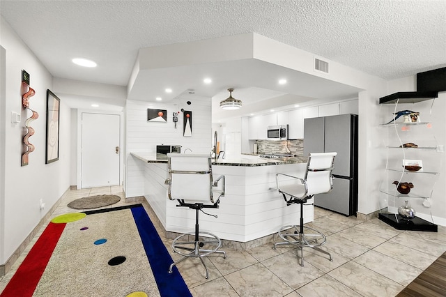 kitchen featuring tasteful backsplash, visible vents, white cabinets, a kitchen breakfast bar, and stainless steel appliances