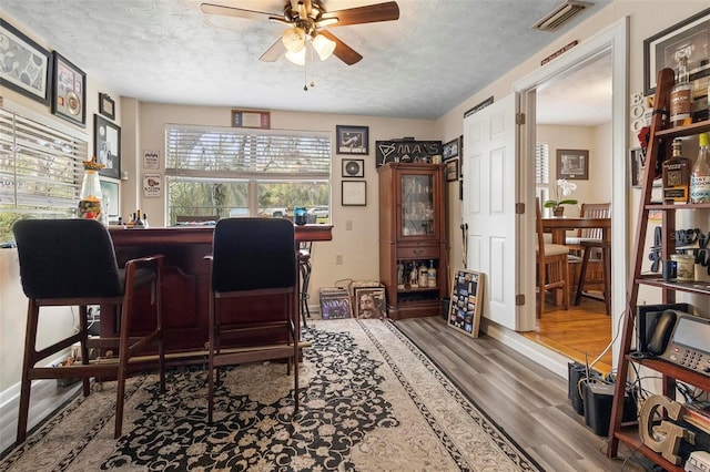 office area with a textured ceiling, ceiling fan, wood finished floors, and visible vents