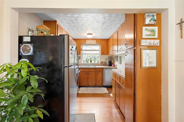 kitchen with a textured ceiling, stainless steel appliances, a sink, light countertops, and brown cabinets