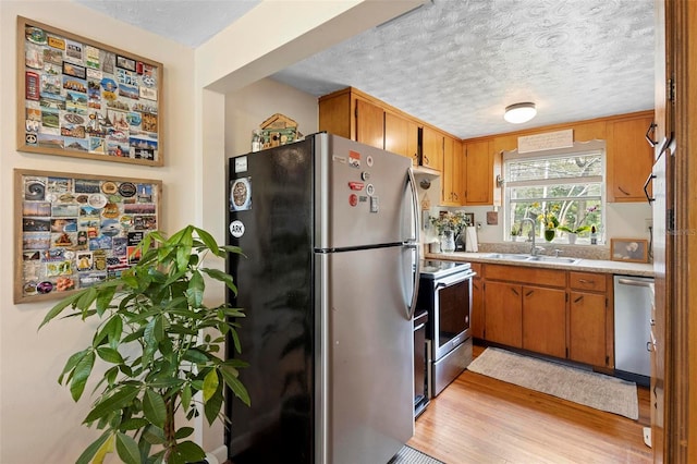 kitchen with appliances with stainless steel finishes, light countertops, a textured ceiling, light wood-type flooring, and a sink