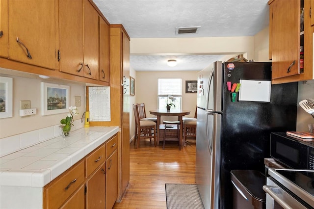 kitchen with tile countertops, black microwave, a textured ceiling, visible vents, and light wood-type flooring