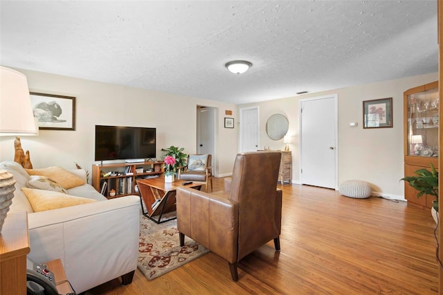 living area with a textured ceiling, light wood-type flooring, and baseboards