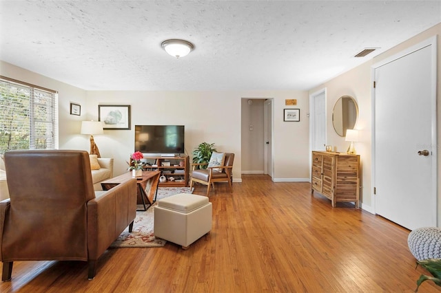 living room featuring light wood finished floors, baseboards, visible vents, and a textured ceiling