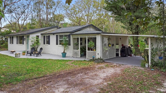 rear view of property with a yard, an attached carport, brick siding, and driveway