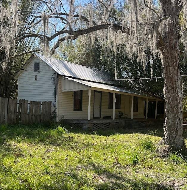 view of front facade with covered porch, a front lawn, fence, and metal roof