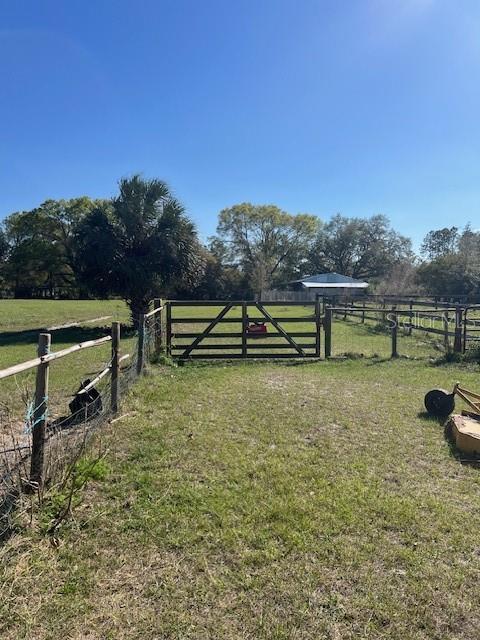 view of gate with fence, a lawn, and a rural view