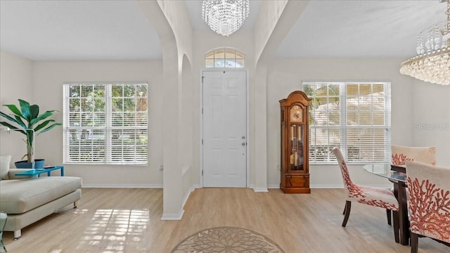 entryway with baseboards, arched walkways, an inviting chandelier, and wood finished floors