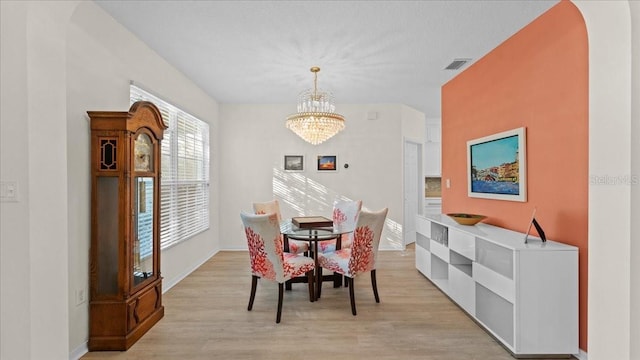 dining space featuring baseboards, visible vents, light wood-style flooring, arched walkways, and a chandelier