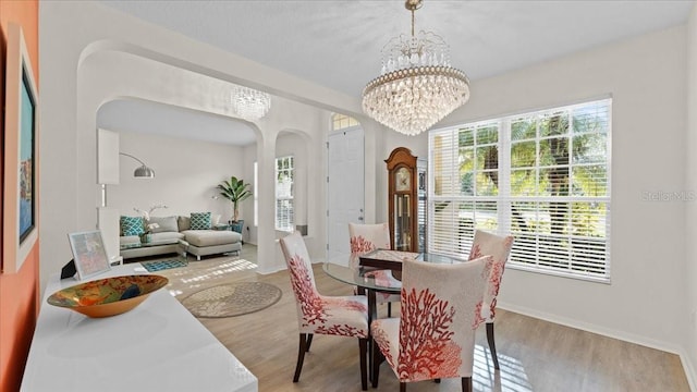 dining area with baseboards, wood finished floors, arched walkways, and a chandelier