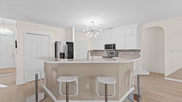 kitchen with light wood finished floors, light countertops, decorative backsplash, an inviting chandelier, and stainless steel appliances