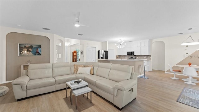 living area with baseboards, visible vents, an inviting chandelier, arched walkways, and light wood-type flooring