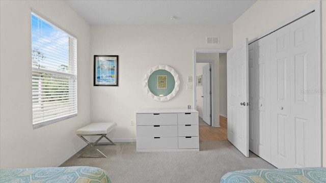 bedroom with a closet, visible vents, light colored carpet, and baseboards