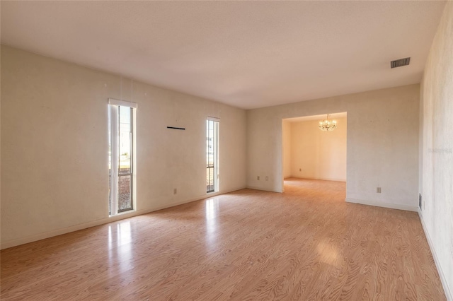 spare room with baseboards, wood finished floors, visible vents, and a notable chandelier