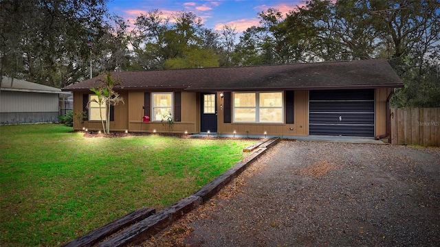 ranch-style home featuring an attached garage, fence, a front lawn, and gravel driveway