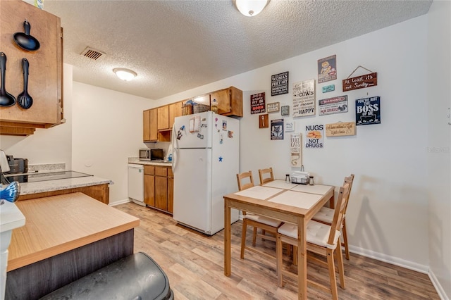 kitchen with a textured ceiling, white appliances, visible vents, light countertops, and light wood-type flooring