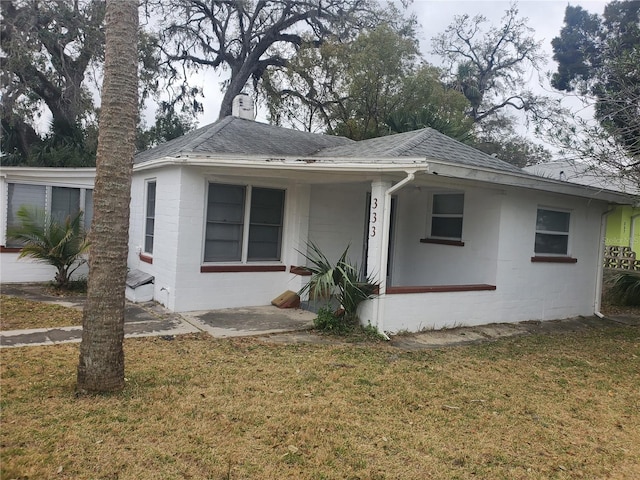 view of front facade with roof with shingles, a front yard, and concrete block siding