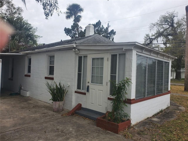 exterior space featuring roof with shingles, a chimney, and concrete block siding