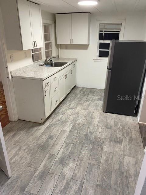 kitchen featuring light wood finished floors, light countertops, freestanding refrigerator, white cabinetry, and a sink