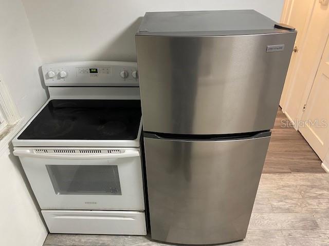 details featuring freestanding refrigerator, light wood finished floors, and white range with electric cooktop