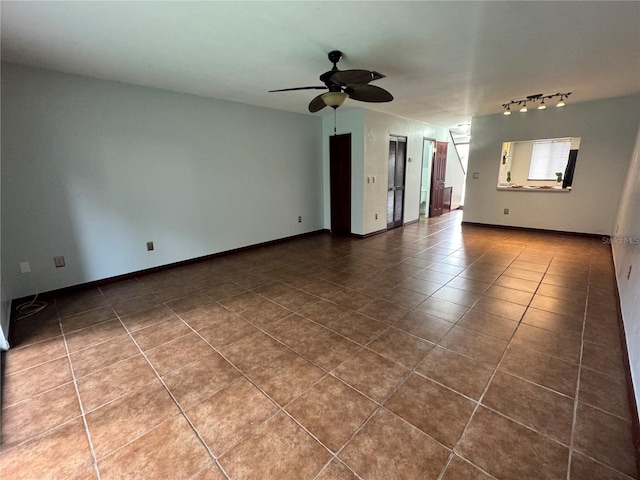 empty room with ceiling fan, baseboards, track lighting, and dark tile patterned flooring