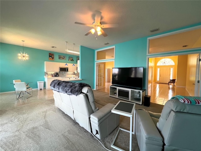 living area featuring ceiling fan with notable chandelier, a textured ceiling, visible vents, and baseboards