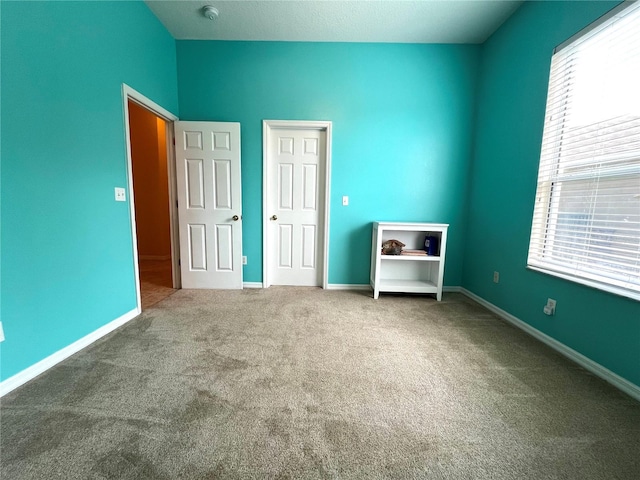 unfurnished bedroom with lofted ceiling, carpet, multiple windows, and baseboards