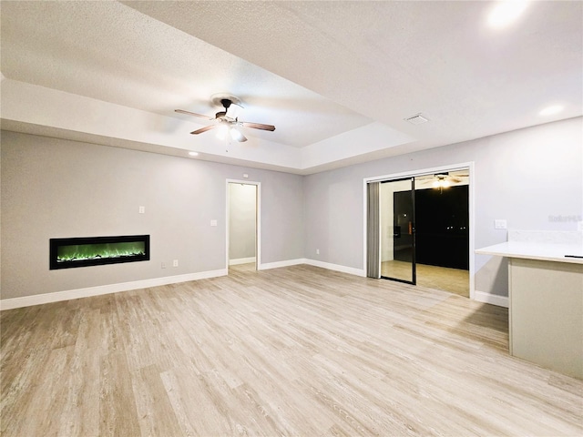 unfurnished living room with light wood-style floors, baseboards, a tray ceiling, and a glass covered fireplace