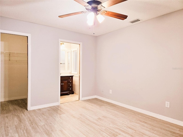 unfurnished bedroom with a walk in closet, a closet, visible vents, and light wood finished floors