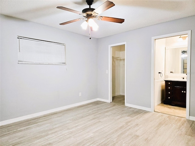unfurnished bedroom with a walk in closet, a closet, ensuite bathroom, light wood-type flooring, and baseboards
