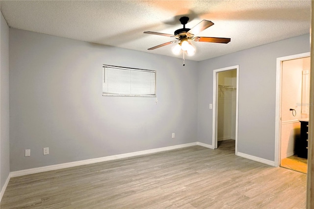 unfurnished bedroom with a textured ceiling, baseboards, a closet, light wood-type flooring, and a walk in closet