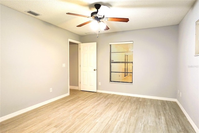 empty room with light wood-type flooring, visible vents, ceiling fan, and baseboards