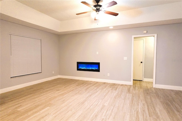 interior space with light wood-style floors, a glass covered fireplace, baseboards, and a ceiling fan